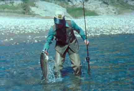 A man pulls a large Masheer fish from a river as he fishes.